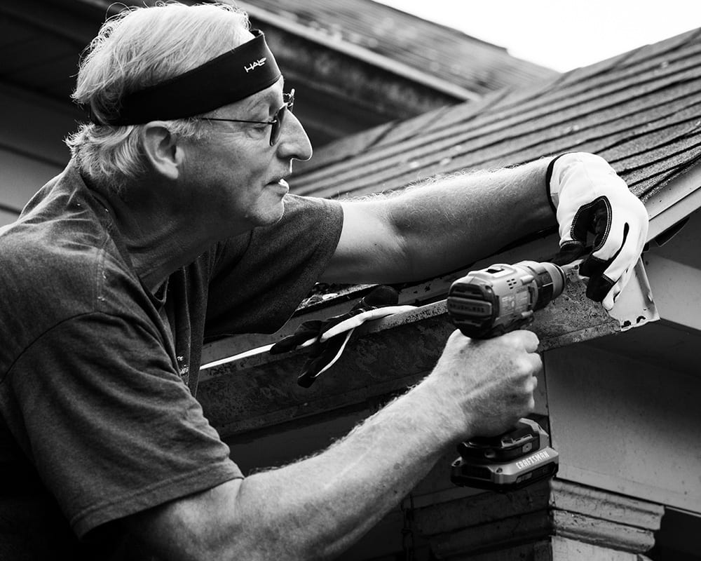 A man holding a drill works on a roof